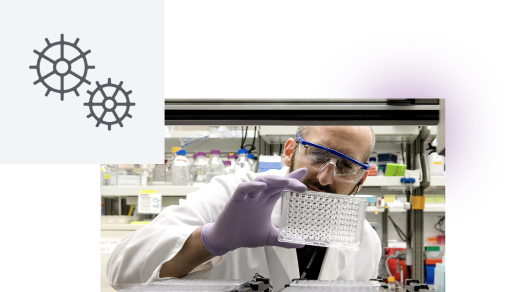 A scientist in a lab examining a well plate with gear icons to the side.