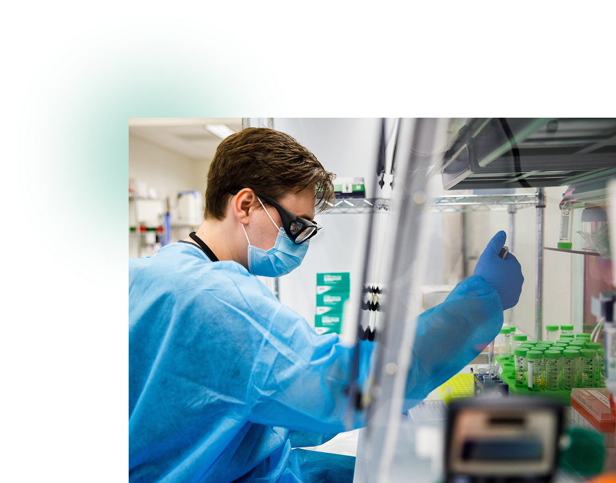 Person in protective gear pipetting in a laboratory with green-capped vials.