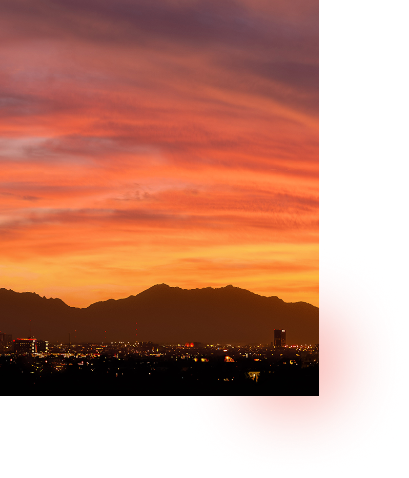 A sunset over a city with a mountain range silhouetted against orange and pink skies.