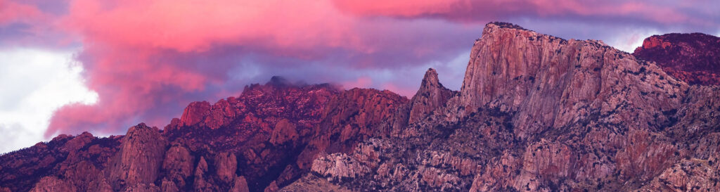 Pink and purple sunset over a rugged mountain range with dramatic clouds.